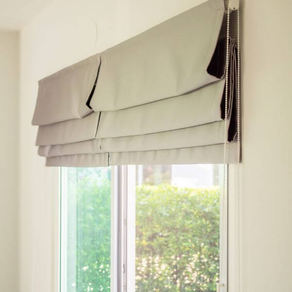 Light grey Roman blind partially raised with neat horizontal folds and a side chain control, fitted cleanly within the window recess, installed by Blinds and Shutter Guys Newcastle.