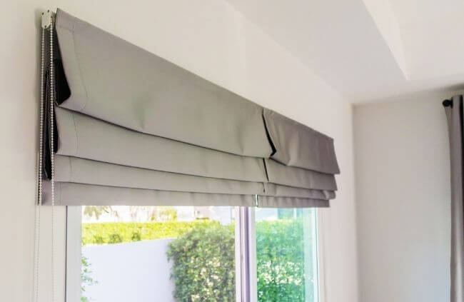 Modern light grey Roman blind neatly stacked at the top of the window with a slim chain control, fitted cleanly inside the recess, installed by Blinds and Shutter Guys Newcastle.